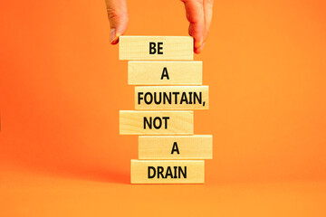 Be fountain not drain symbol. Concept words Be a fountain not a drain on wooden block. Beautiful orange table orange background. Businessman hand. Business be fountain not drain concept. Copy space.