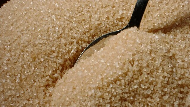 Scooping pure brown sugar with spoon. Close up slow motion sugar background. Limiting sugar is paramount to safeguarding against several chronic conditions disease, including obesity and diabetes.