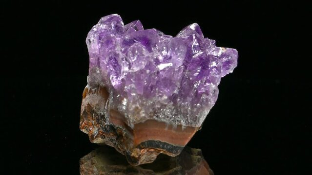 Amethyst (purple quartz) crystals on a matrix of rock strata rotating slowly against a black background