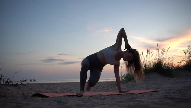 Female instructor flexible slender body training yoga pose asana, uses a mat for exercises against the background of sunset.  Mental health and an active lifestyle.