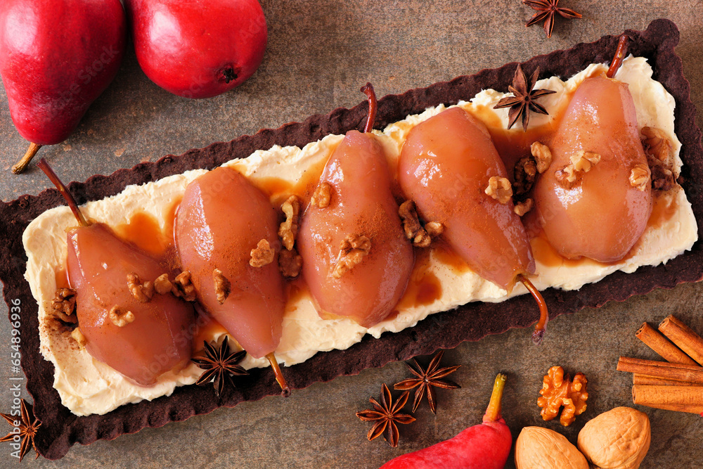 Poster Spice poached pear tart with caramel on a chocolate and cream base. Overhead view table scene on a dark stone background.