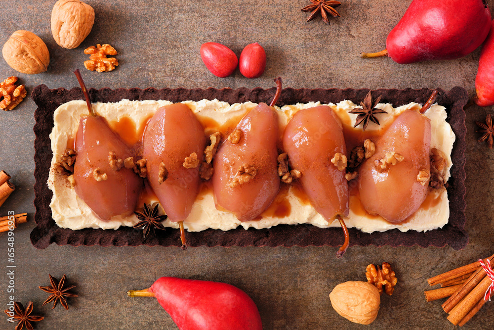 Poster Spice poached pear tart with caramel on a chocolate and cream base. Above view table scene over a dark stone background.
