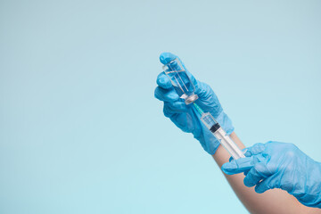 The doctor's hand wears a medical glove holding a syringe while taking a liquid vaccine from a vial about to be injected. Injection vaccination concept