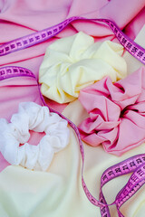 three white, pink and yellow scrunchies and pink measuring tape on soft yellow and pink fabric. Haistyle concept	