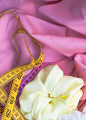 concept with pink and yellow measuring tape and accessories for hair on pink soft fabric. Place for art. Yellow scrunchie. Beauty concept	