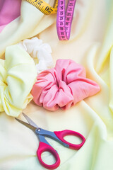 sharp red scissors, three white, yellow and pink scrunchies for hair on yellow fabric. Art and creating beauty