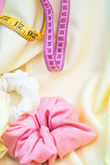 pink and white scrunchies on thin yellow fabric around pink measuring tapes. Beauty concept	