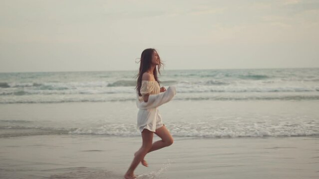 Happy asian woman running on sea beach, Slow motion, Smiling cheerful lady have fun on seashore enjoy beautiful nature.