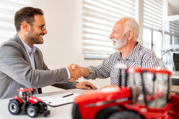 Investment in agricultural machinery and farming equipment. Farmer and dealer shaking hands and...