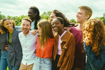Multiracial students (20-30) embrace in a sunny park, laughing, showcasing unity, diversity, and...