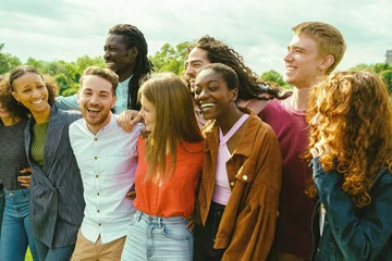 Foto op Plexiglas Multiracial students (20-30) embrace in a sunny park, laughing, showcasing unity, diversity, and tolerance. Multiethnic group of millennials having fun outdoors © Lomb