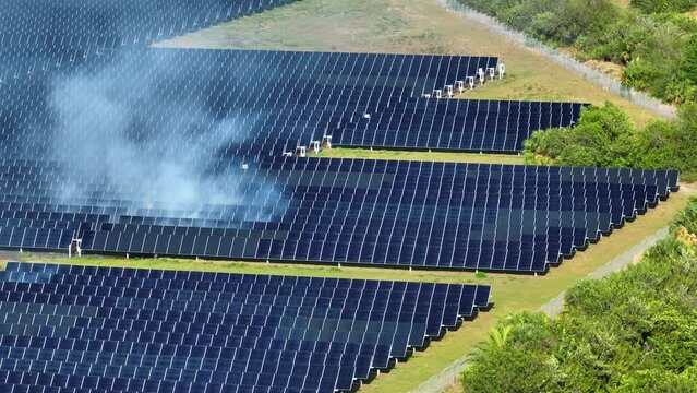 Aerial view of fire burning at big sustainable electric power plant with many rows of solar photovoltaic panels for producing clean electrical energy. Seasonal wildfire at critical infrastructure