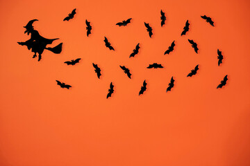 Wooden cutouts of a witch and bats isolated on a orange background.
