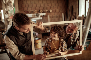 Multigenerational family of male carpenters teaching their youngest one the ways in a carpentry shop