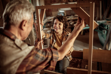 Fototapeta na wymiar Senior male carpenter showing his grandson a wood frame in a carpentry shop