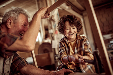 Senior male carpenter teaching his grandson how to use a hammer in a carpentry shop
