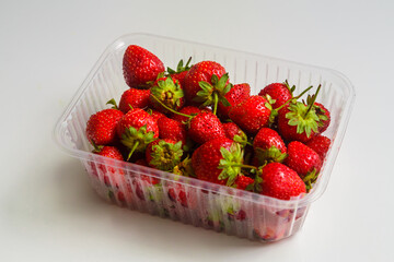 Fresh red strawberries with green sprigs in a transparent plastic container on a white table