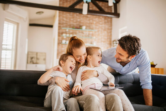 Happy young family bonding and having fun on the couch at home - Powered by Adobe
