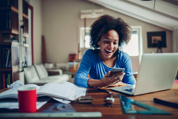 Young mixed woman using her smartphone while studying at home