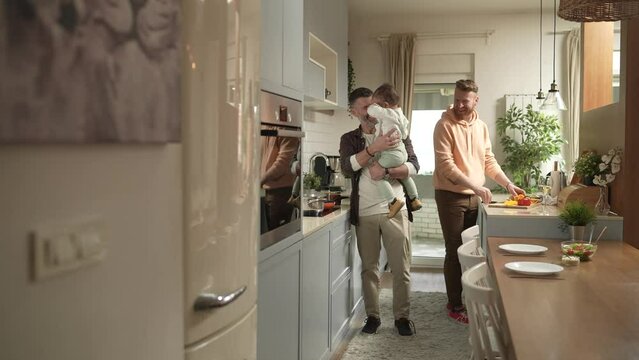Young male gay couple preparing an organic dinner with their child in the kitchen at home