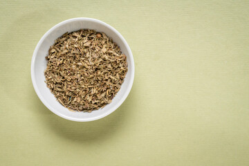 oregano dried herb - small ceramic bowl on textured paper with a copy space, top view