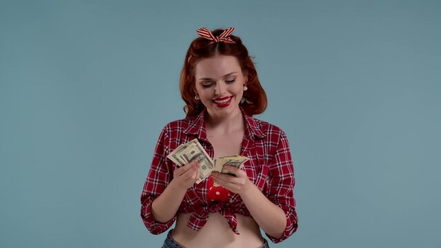 In the picture on a blue background, a young redheaded woman with bright makeup. She counts, counts money. She likes it, shes happy, happy and happy. Counting the salary, the pay.