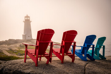 Four Adirondack chairs facing Peggy's Cove Lighthouse during foggy sunset evening, Nova Scotia, Canada. Photo taken in September 2023.