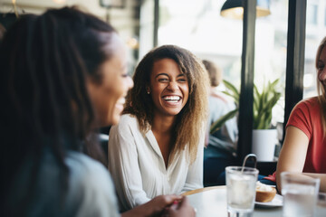 Happy smiling female friends sitting in a café laughing and talking during a lunch break