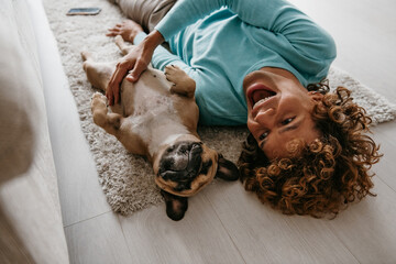 Top view of happy young man petting his cute dog while lying on the floor at home together