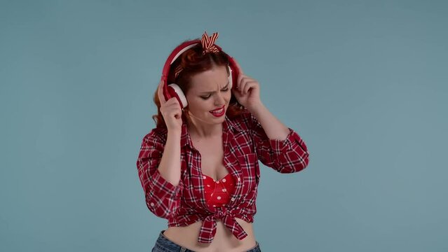 In the picture on a blue background, a young woman with a bright makeup. She puts on cordless red headphones. Listens to music singing and dancing. Enjoys and enjoys the track, the song.