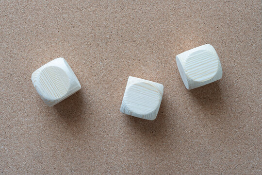 three plain wood crafting dice on cork