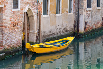 Picturesque idyllic scene with a yellow boat docked or moored on the water canals in Venice, Italy.