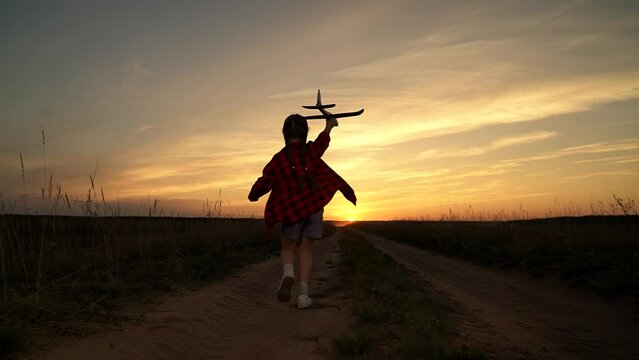 Little girl with toy aeroplane enjoys dream about flights in sunset meadow