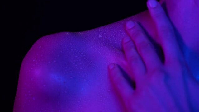 Closeup shot of woman touching body part in neon light, neck collarbone area skin after shower in water drops.
