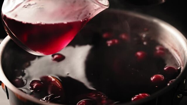 A person scoops mulled wine into a glass mug with a ladle from a saucepan. Hot mulled wine with oranges cranberries and spices. Stock video 4k