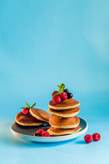 Appetizing pancakes with berries and powdered sugar on blue background