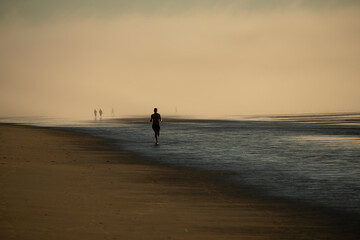 Fototapeta na wymiar The coast of the Atlantic Ocean at dawn in heavy fog. Silhouettes of people on the shore walking and jogging at dawn. USA. Maine.
