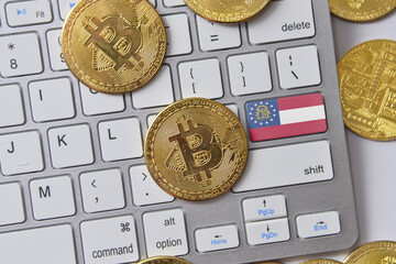 flag of georgia state on the keyboard with bitcoin coins on a grey background.