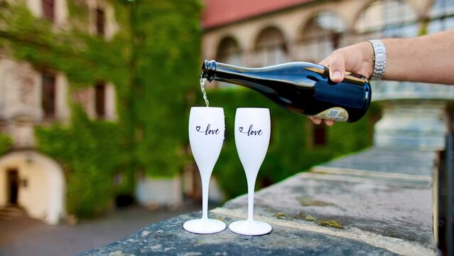 Pouring prosecco from a bottle into two glasses with a view on castle. 