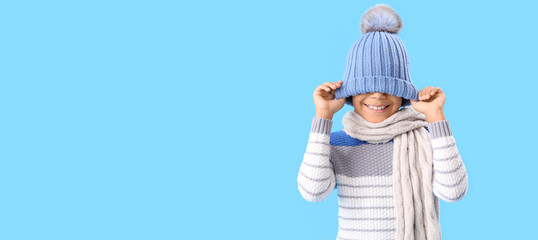 Cute African-American boy in warm winter clothes on blue background with space for text