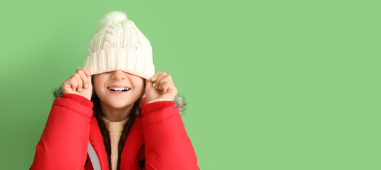 Funny little girl in winter hat and warm coat on green background with space for text