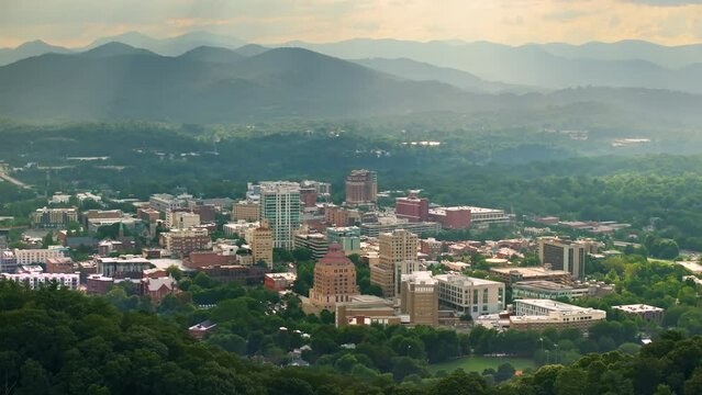 Aerial view of USA travel destination. Asheville city in North Carolina with high downtown buildings and Appalachian mountain hills in distance at sunset