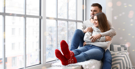 Happy couple in winter clothes sitting on window sill at home