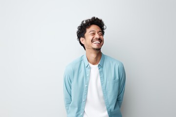 A cheerful man with curly hair wearing a blue shirt smiles at the camera - obrazy, fototapety, plakaty