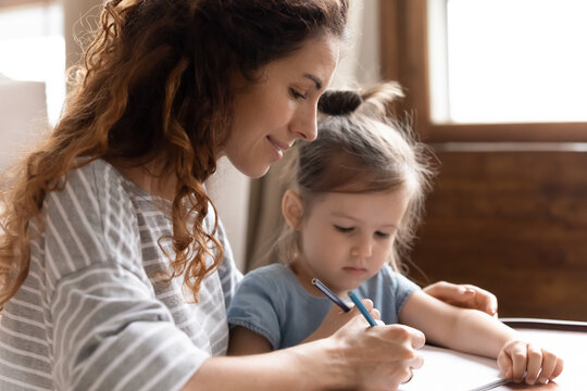 Smiling young mother and cute little preschooler daughter have fun drawing pictures at home together, caring millennial mom or nanny play painting with colorful pencils enjoy weekend with small girl