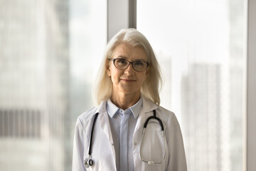 Positive senior medical therapist woman in glasses and white coat head shot portrait. Female...