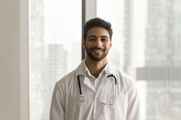 Happy handsome young Arab doctor man wearing white uniform coat and stethoscope posing for...