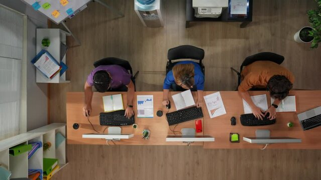 Call center or sales department. Top view of workers working at the desks on computers in headsets, reading documents, giving high five