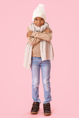 Freezing African-American boy in winter clothes on pink background
