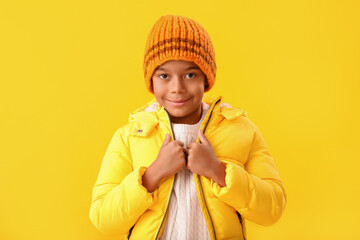 Cute African-American boy in warm winter clothes on yellow background